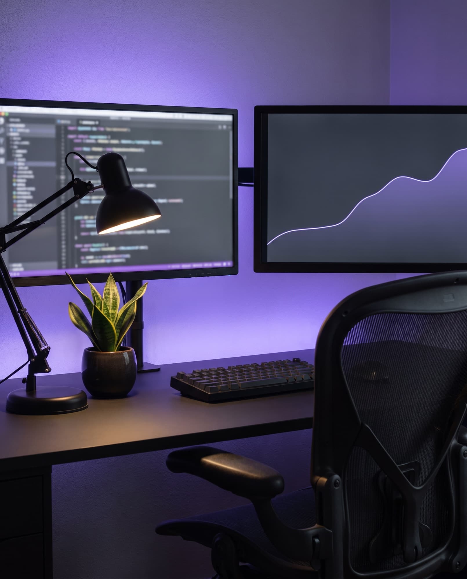 Mesa de desenvolvedor à noite, com dois monitores e uma luz violeta na parede